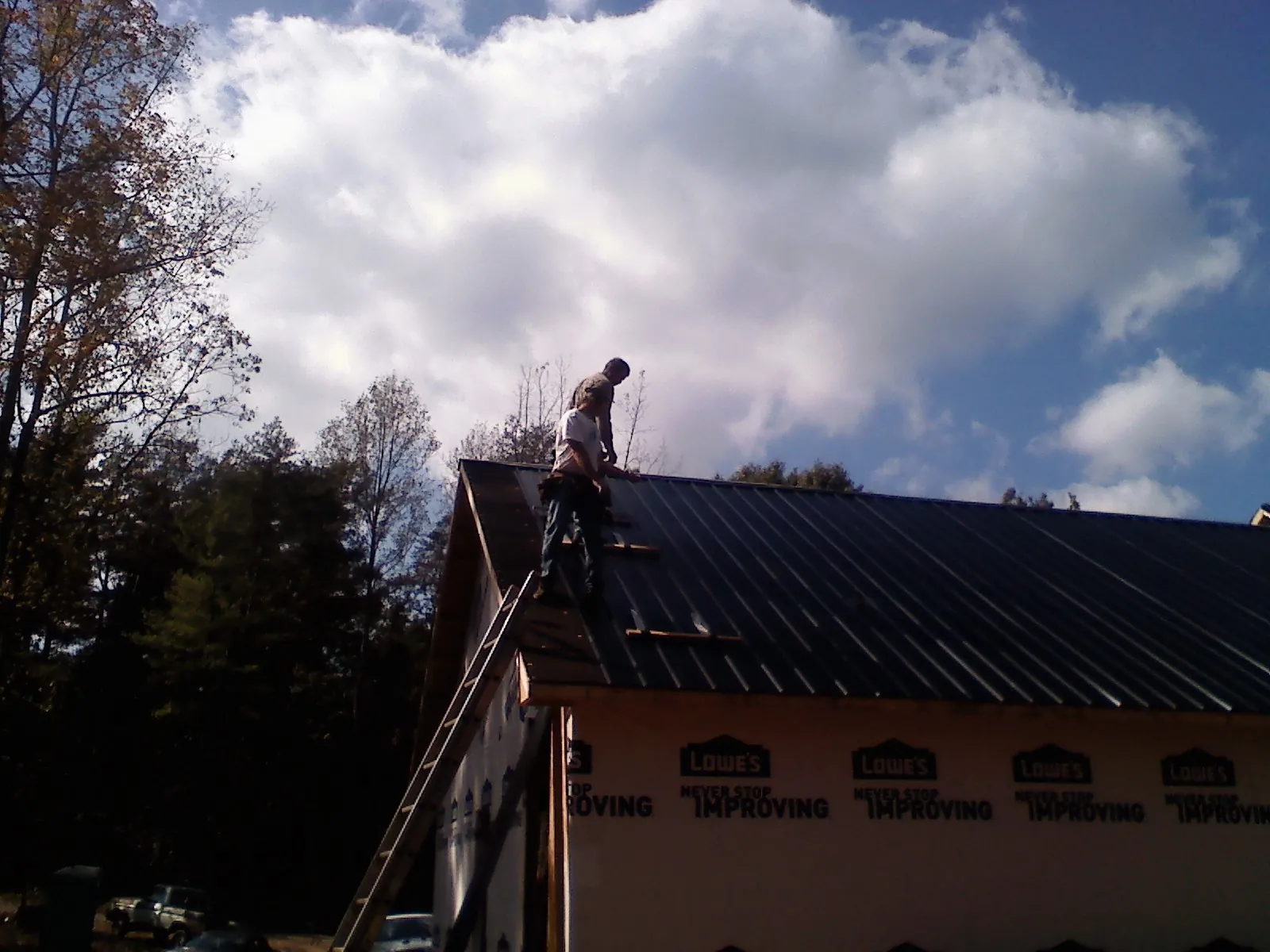 Roofer fastening dark metal panels high against a cloudy sky, from a Roof Inspection job in Springville